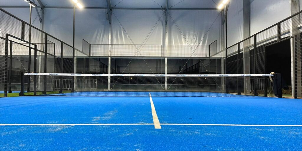 Terrain de padel panoramique construit par Padelcourt, AST Roissy-en-Brie, Roissy-en-Brie (77) : Une piste de nuit, éclairage allumé, filet marqué Padelcourt