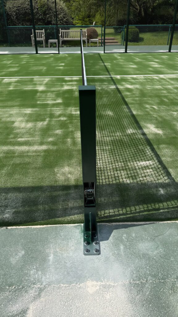 Terrain de padel panoramique construit par Padelcourt, chez un particulier du Calvados (14) : Le poteau de filet, fixé au sol en bord de piste